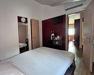 Interno di una camera d’albergo con divano-letto matrimoniale, specchio e armadio aperto.